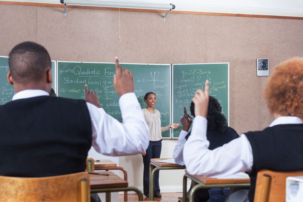 Medium POV of the back of students with their hands raised in classroom, Cape Town, South Africa