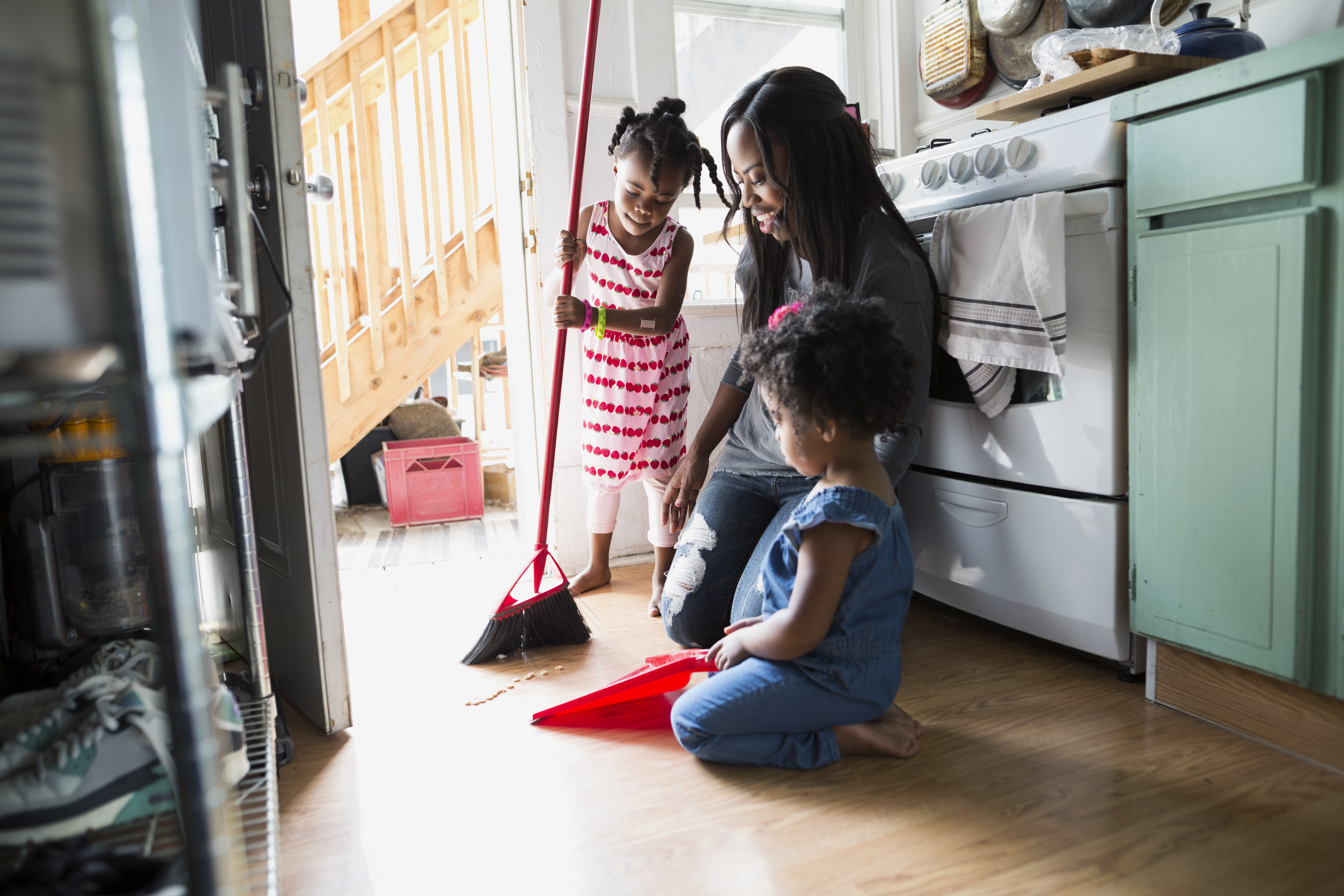 Daughters helping mother sweep kitchen floor