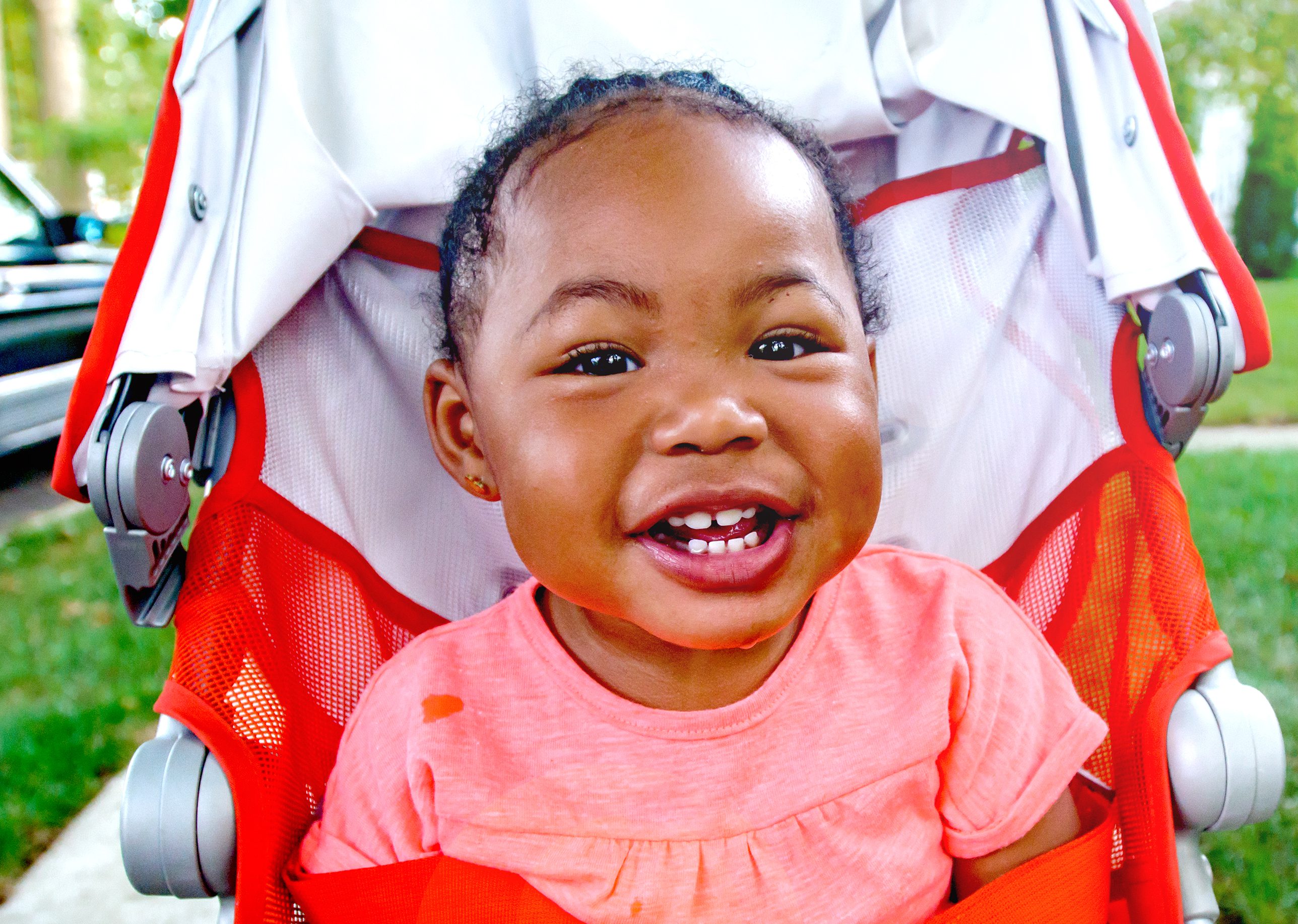 Happy baby girl in pushchair on suburban sidewalk, portrait