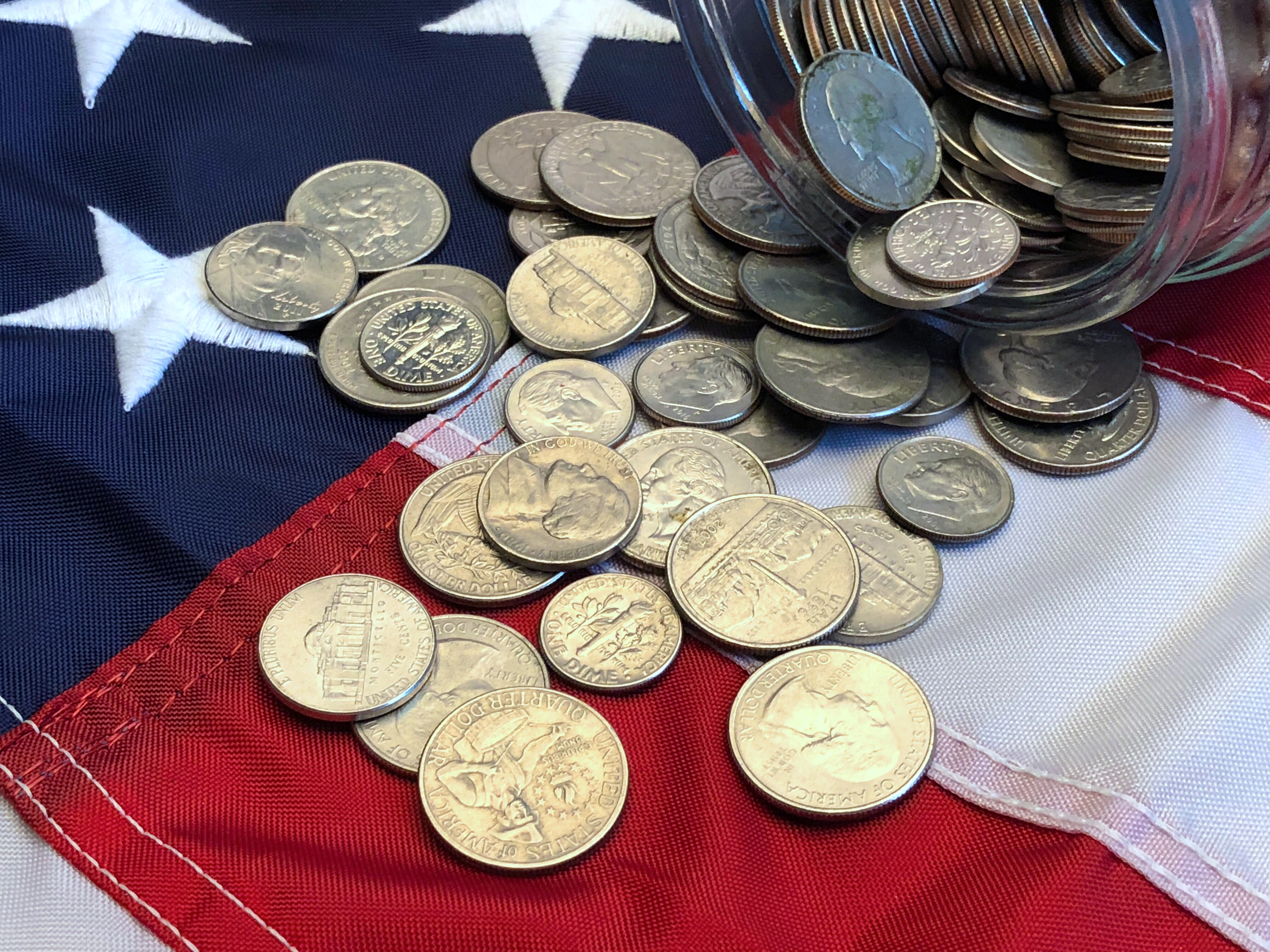 American quarters, nickels and dimes spilling from a jar onto an American flag