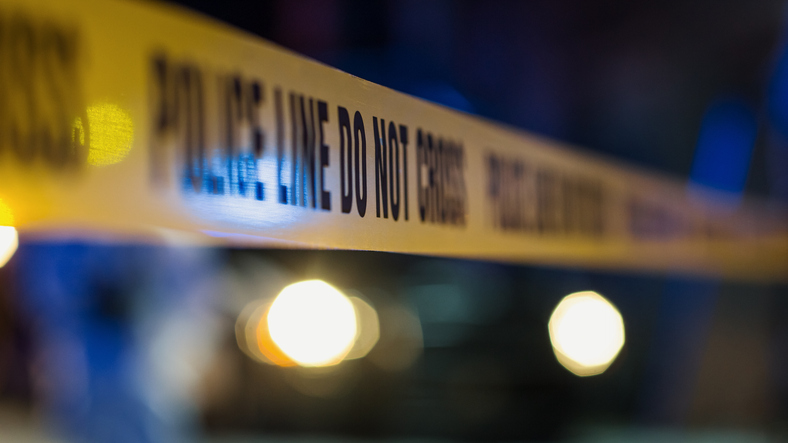 Yellow Tape Showing Text Police Line Do Not Cross Restricting a Crime Scene Area At Night. Close Up Aesthetic Shot with Bokeh Effect. Text Blurred. Criminal on the Loose Strikes Again