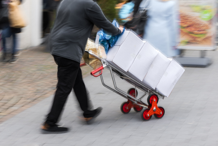 Man pushes a hand truck with packages through the pedestrian zone in a city